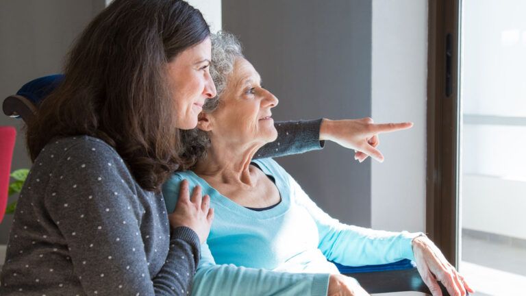 Caregiver and senior woman looking out of a window