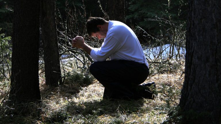 A woman kneels in prayer outdoors