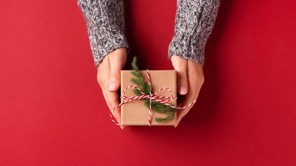 Hands holding a faith gift for Christmas 2022 on a red background