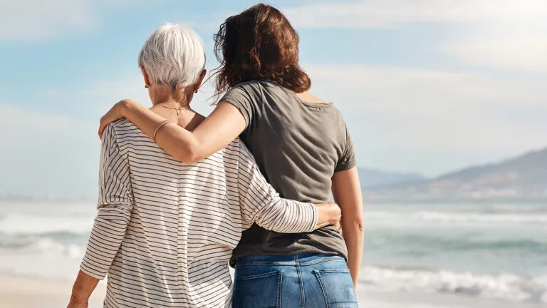 An adult woman and her senior mother walk along a beach