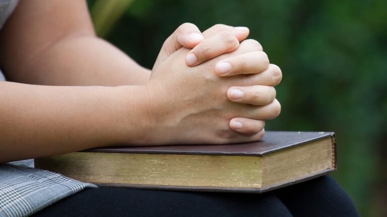 A woman's hands clasped in prayer rest on a Bible