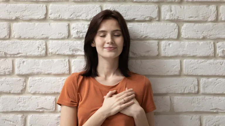 Woman against a white brick wall saying a prayer of gratitude