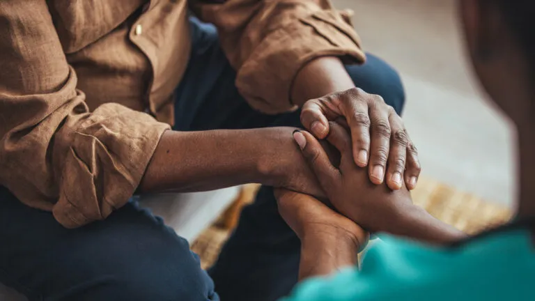 Female caregiver holding senior man's hands.