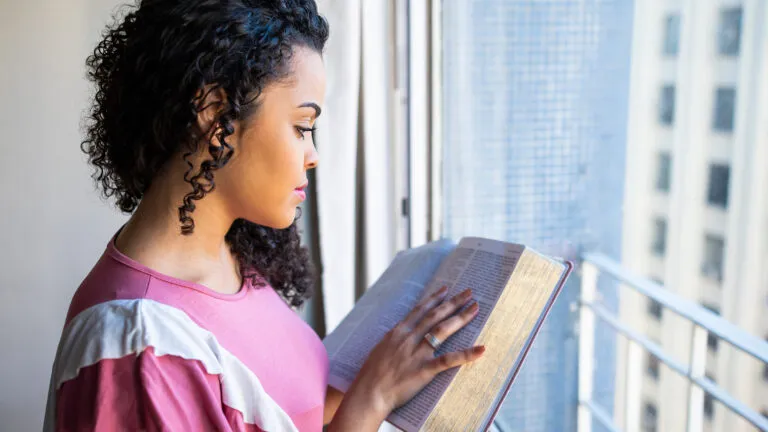 A woman reading by the window to develop her daily devotional habit