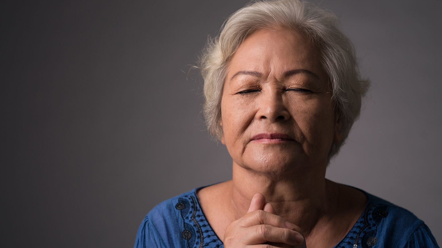 A woman clasps her hands in prayer