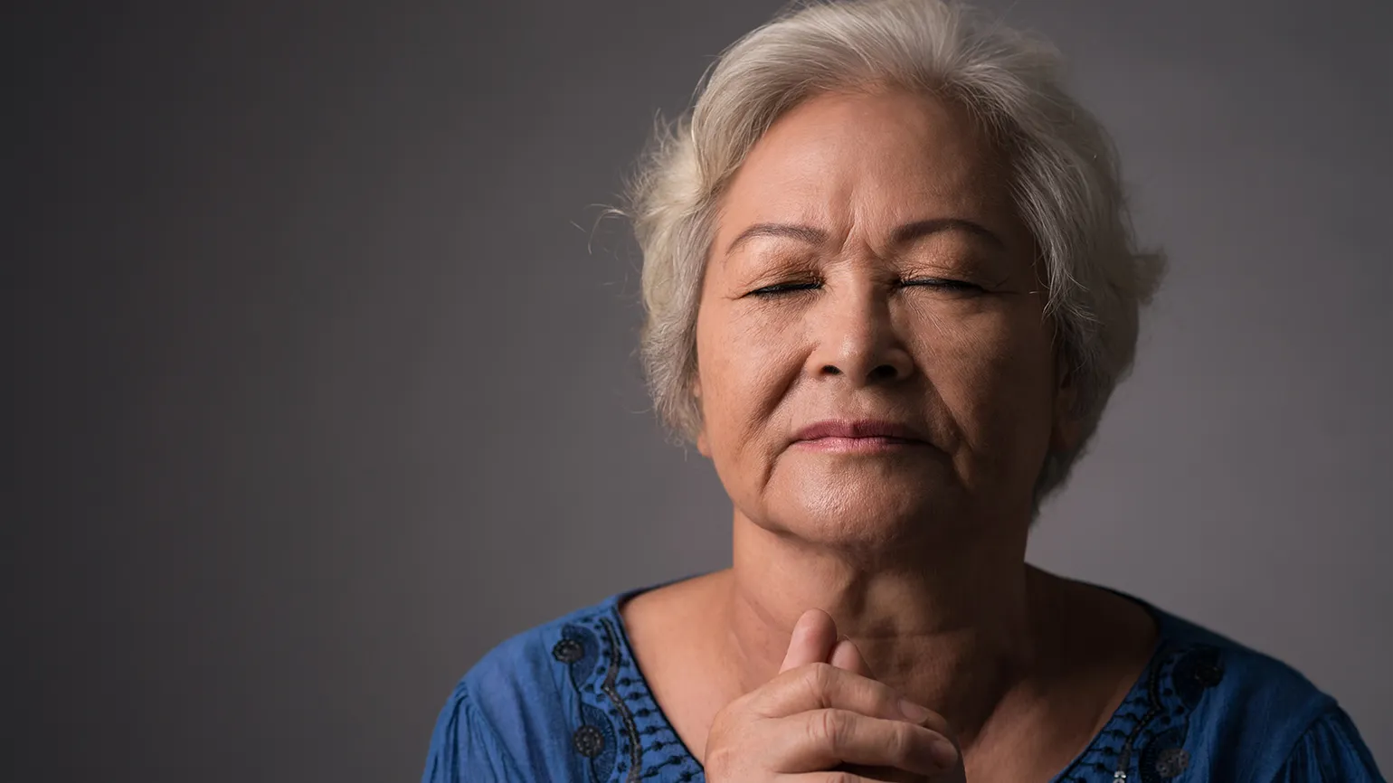 A woman clasps her hands in prayer